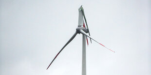 Windrad mit abgebrochenem Flügen vor grauem Himmel