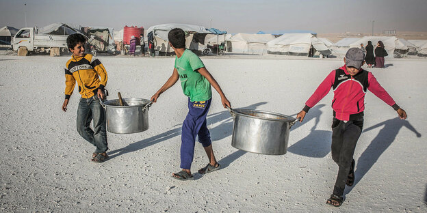Syrische Kinder tragen in einem Flüchtlingslager, leere Töpfe