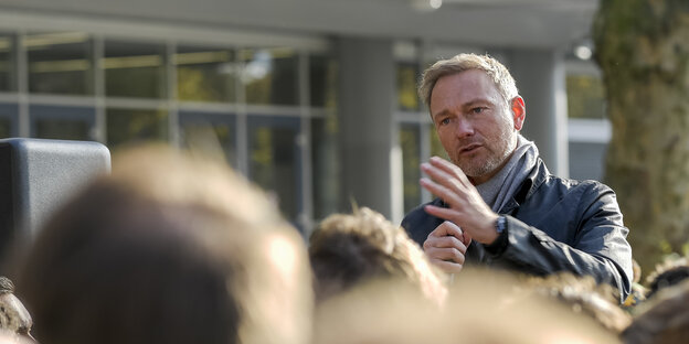 Christian Lindner spricht gestikulierend vor unscharfen Köpfen Christian Lindner spricht gestikulierend vor unscharfen Köpfen