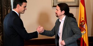 Pedro Sanchez und Pablo Iglesias machen Shakehands vor der spanischen Flagge