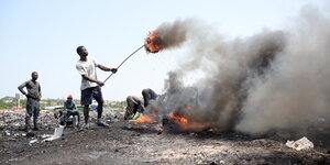 Mehrere Männer stehe auf einem Schrottplatz in Ghana und verbrennen alte Kabel und Elektroschrott. Die Luft ist voll mit grauem Dampf
