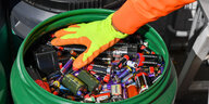Eine Hand mit Handschuh greift in eine grüne Tonne, die mit Batterien gefüllt ist