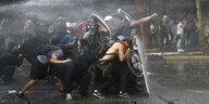 Auf einer Straße in Chile schützen sich Demonstrant*innen vor einem Wasserstrahl