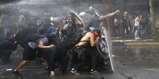 Auf einer Straße in Chile schützen sich Demonstrant*innen vor einem Wasserstrahl