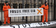 Zwei Menschen in Ganzkörperanzügen halten einen Banner hoch, auf dem steht: "Fossil free EIB"