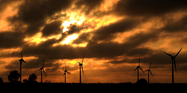 Windkraftanlagen vor einem wolkigen Himmel mit Abendrot