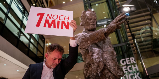 Ein Helfer hält bei der Debatte der Bewerberteams für den SPD-Vorsitz zum Schluss ein Schild hoch, im Hintergrund die Statue von Willy Brandt.