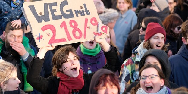 Eine Frau hält auf einer Demonstration ein Schild hoch, auf dem steht: "Weg mit § 218/9"