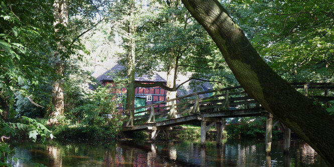 Ein Haus steht am Wasser, eine Brücke führt hinüber