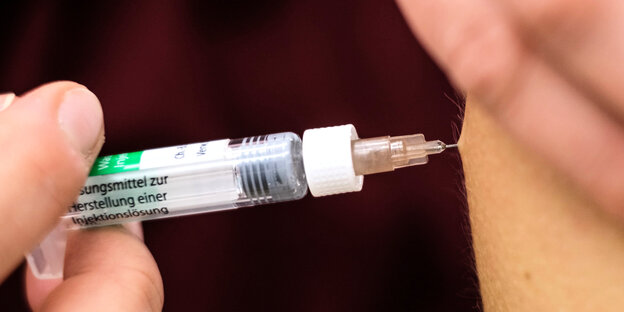 Eine Spritze wird zur Impfung in einen Oberarm gestochen.