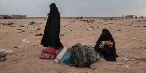 Zwei Frauen im Tschador sthene in einer mit Müll bedeckten Wüste