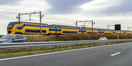 Ein gelb-blauer Zug fährt neben einer Autobahn
