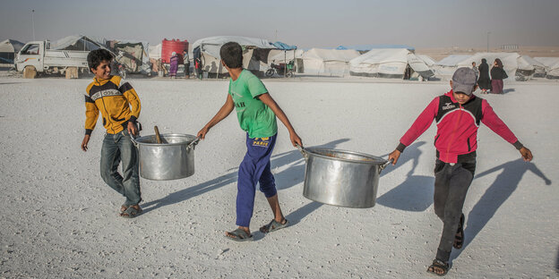 Kinder tragen leere Kochtöpfe in Flüchtlingslager