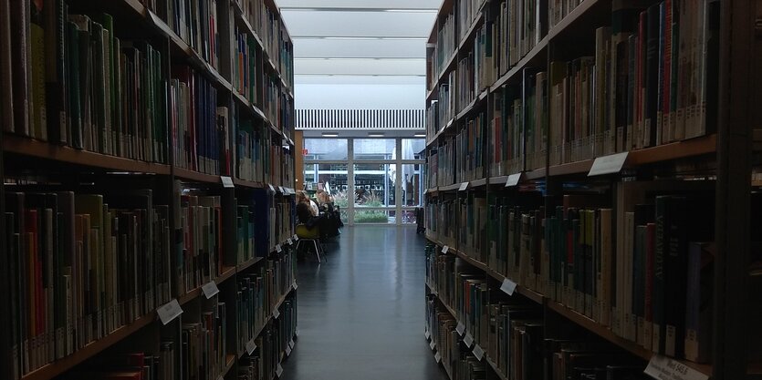 Stadtbibliothek. Blick durch einen Gang in der Stadtbibliothek Breite Str. 30, links und rechts gesäumt von vollen Bücherregalen. Am Ende des Ganges befindet sich der große, helle Lesesaal.