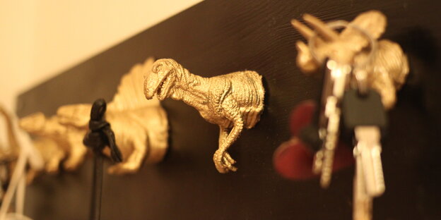 Gold angemalte Dinosaurierköpfe an einem Holzbrett befestigt, an einem hängt ein Schlüssel Gold angemalte Dinosaurierköpfe an einem Holzbrett befestigt, an einem hängt ein Schlüssel