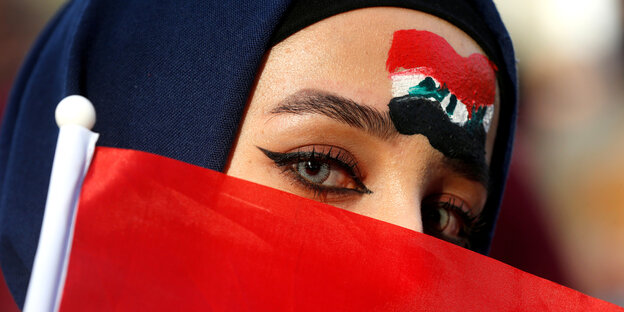 eine Frau, die ihr Gesicht hinter einer irakischen Flagge verbirgt
