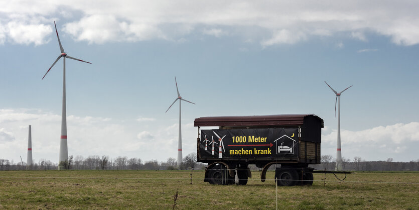 Ein Bauwagen steht vor Windrädern. Drauf steht, dass alles unter einem Kilometer Abstand krank macht