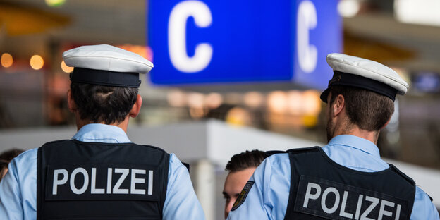 Zwei Männer in Polizeiuniform am Flughafen, von hinten fotografiert.