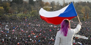 Eine Frau schwenk die tschechische Flagge, sie steht erhöht, unter ihr haben sich Menschenmassen versammelt