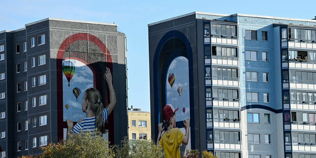 Große Wandgemälde auf Plattenbauten, eine Frau und ein Kind schauen auf Ballons
