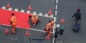 Arbeiter in orangen Anzügen markieren einen Radweg