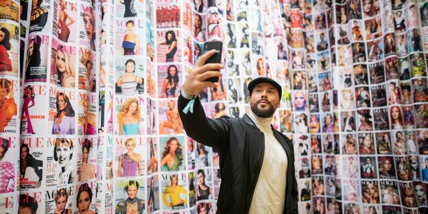 Ein Mann macht ein Selfie vor unzähligen Vogue-Titelbildern