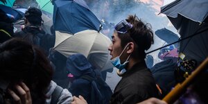 Ein Demonstrant mit hochgezogener Atem- und Augenmaske zwischen Regenschirmen