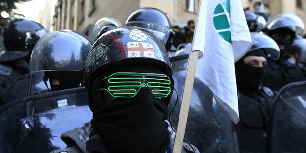 Maskierter Demonstrant mit Helm und Fahne