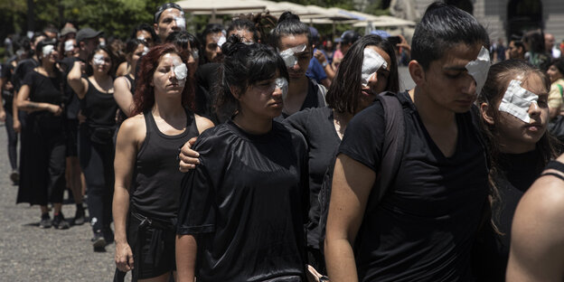 Schwarz gekleidete Menschen demonstrieren mit Pflastern auf den Augen