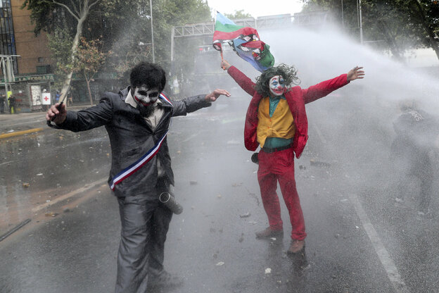 Ein als Joker verkleideter Demonstrant steht im Strahl eines Wasserwerfers auf der Straße