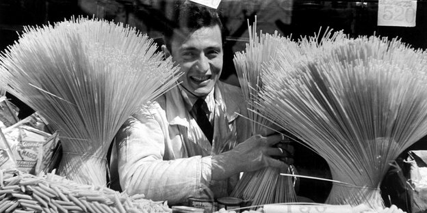 Schwarz-Weiß-Foto eines Verkäufers, der zwischen einer Dekoration aus Spaghetti steht