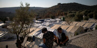 Zwei Männer sitzen Flüchtlingslager, im Hintergrund Zelte