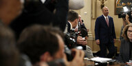 Ein Mann in Anzug betritt einen Raum voller Reportern.