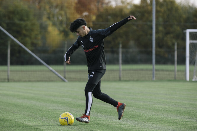 Junger Fussballer mit ausgebreiteten Armen und Ball