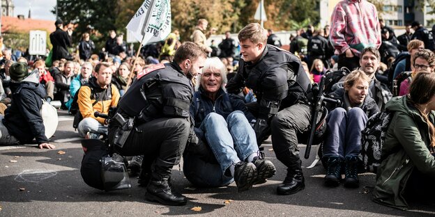 Ein Mann sitzt mit anderen Demonstrierenden von Extinction Rebellion auf dem Boden und wird von der Polizei weggetragen.