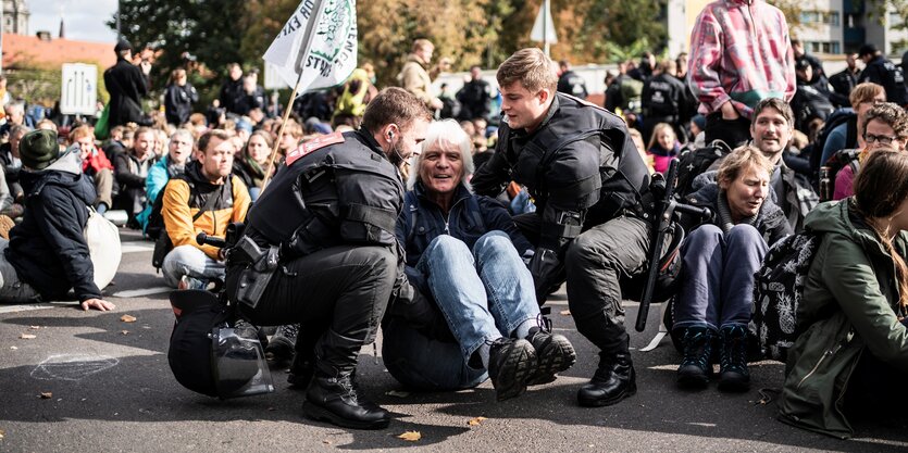 Ein Mann sitzt mit anderen Demonstrierenden von Extinction Rebellion auf dem Boden und wird von der Polizei weggetragen.