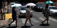 Drei Frauen mit Regenschirmen überqueren eine Straße