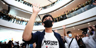Vermummter Demonstrant hebt die Hand hoch, umringt von vielen Menschen, die auch protestieren