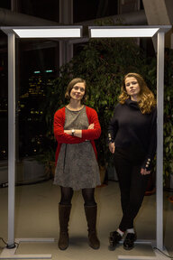 Die zwei Frauen Mahlhaus und Neubauer stehen vor Zimmerpflanzen. rechts und links von ihnen stehen dünne Säulen, an deren oberen Enden viereckige Lampen angebracht sind Die zwei Frauen Mahlhaus und Neubauer stehen vor Zimmerpflanzen. rechts und links von ihnen stehen dünne Säulen, an deren oberen Enden viereckige Lampen angebracht sind