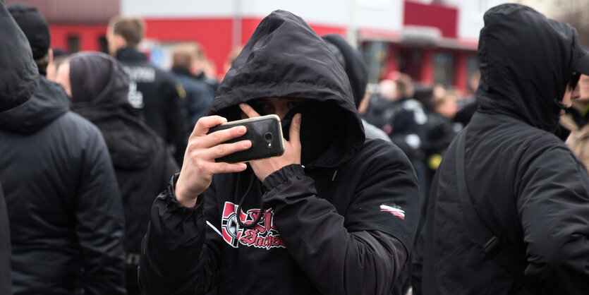 Ein vermummter Mann filmt auf einer Demo mit seinem Handy