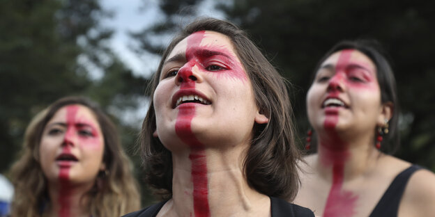 Frauen mit teils rot geschminkten Gesichtern protestieren