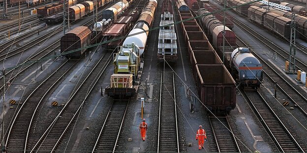 Zwei Arbeiter mit Warnanzügen stehen vor Güterwaggons der Deutschen bahn