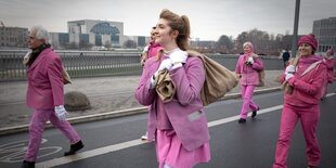 Frauen und Männer in pinker Kleidung laufen über eine Brücke in der Nähe des Kanzleramts.