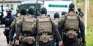 Polizisten aus der Rückenansicht, mit Schutzwesten, Waffen und Helmen