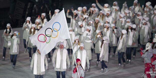 Russische Athleten ganz in Weiß gekleidet schwenken die olympische Fahne bei der olympischer Eröffnungsfeier.