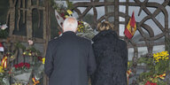 EIn Mann und eine Frau stehen vor einem mit Blumen und spanischen Flaggen geschmückten Tor