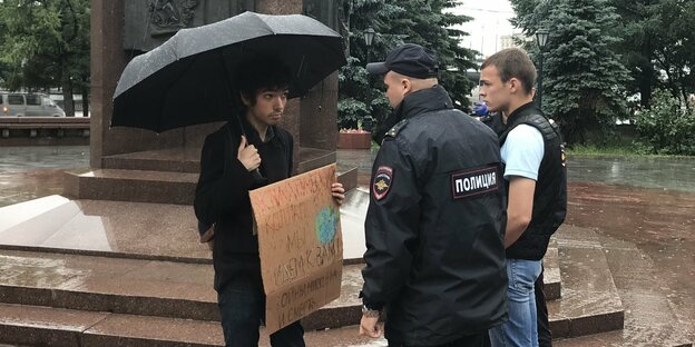 Junger Mann mit Schirm und Schild erklärt sich 2 Sicherheitskräften