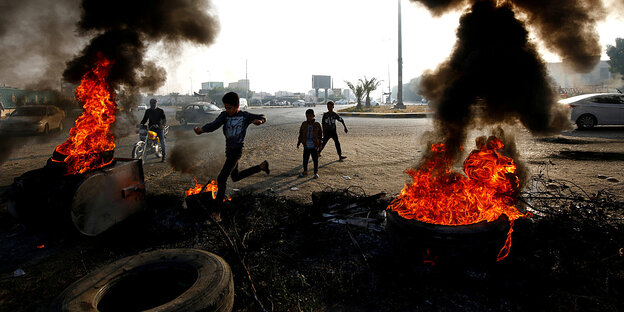 Reifen brennen auf einer Straße, im Hintergrund: rennende Kinder