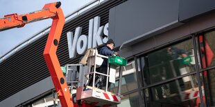 Ein Arbeite auf einem Hubsteiger bringt graue Platten vor dem Namen der Vollkswagen-Halle an.