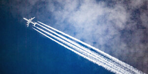 Ein Flugzeug hinterlässt Kondensstreifen am blauen Himmel.